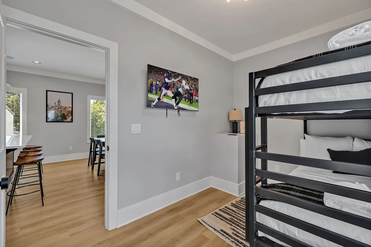 A playful and energetic bunk room with a sturdy bunk bed, sports-themed artwork, a lamp, and a window with natural light. The space is designed for both relaxation and fun, ideal for children or singles.