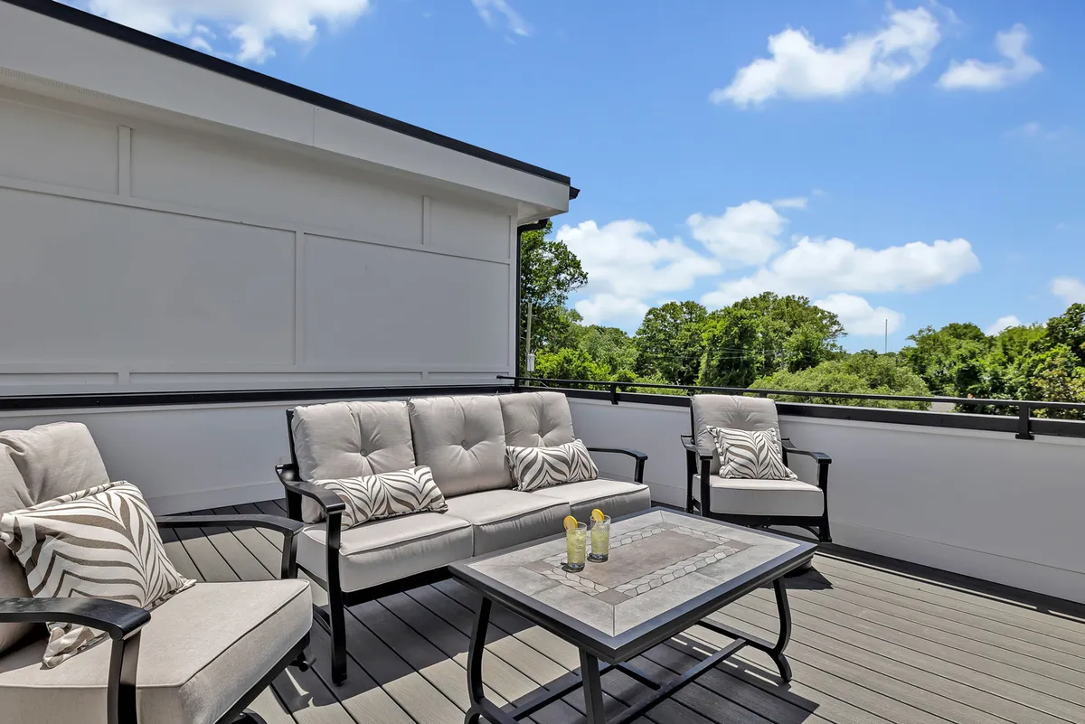 A tranquil rooftop deck with an outdoor seating area and coffee table, surrounded by greenery. The space is bathed in natural light, suggesting a perfect spot for both daytime relaxation and evening celebrations.