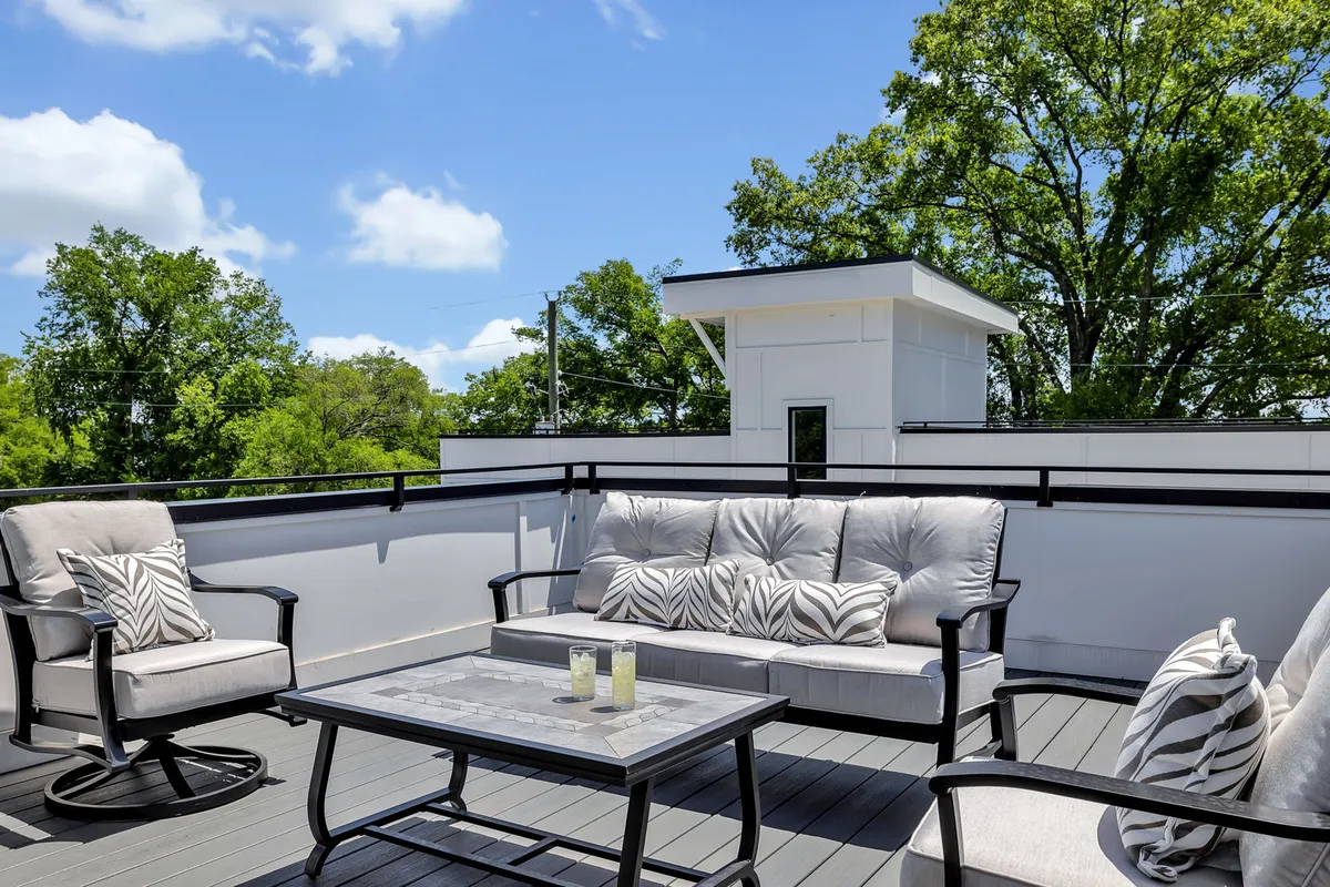 A serene rooftop exterior with comfortable seating, decorative throw pillows, and a coffee table with candles. The evening sky offers a tranquil backdrop, perfect for relaxing or stargazing as a group.