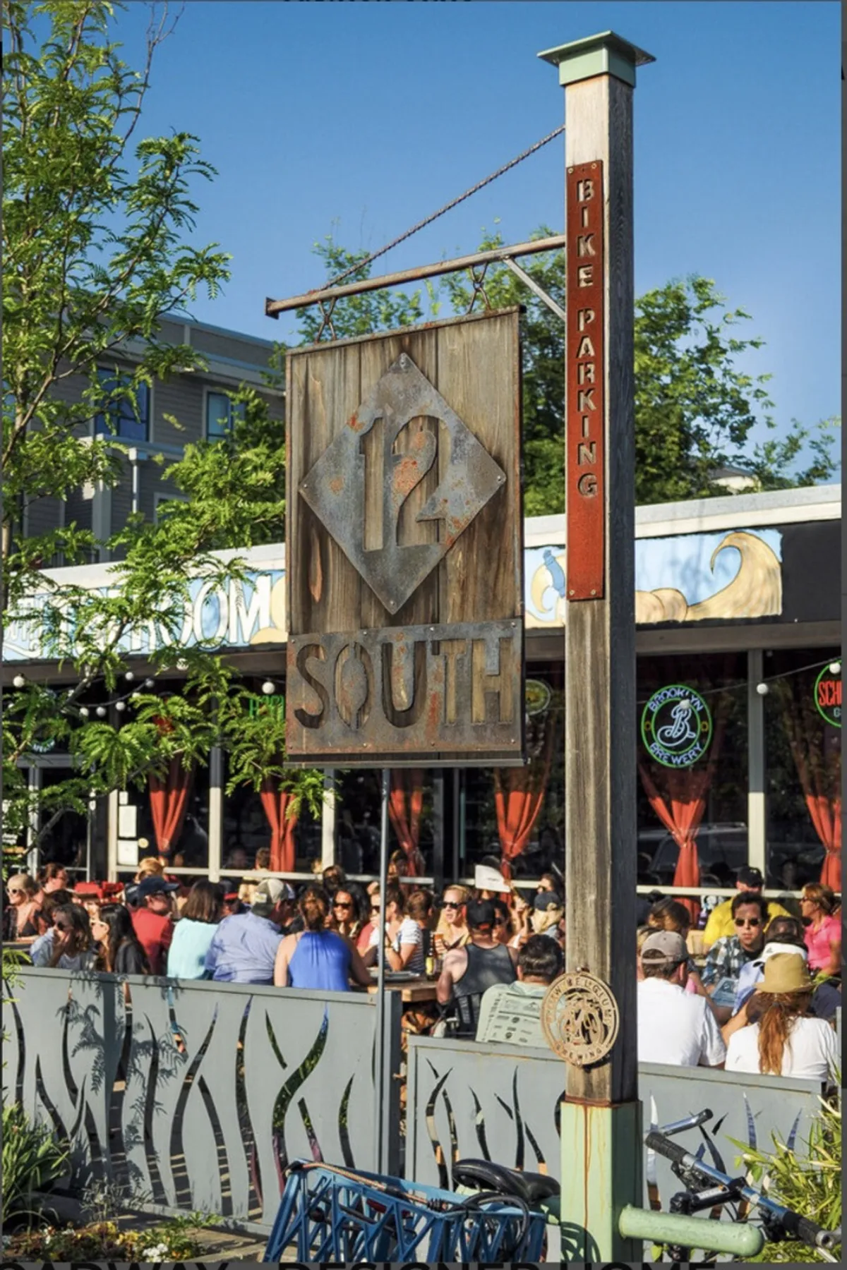 An inviting exterior view of the 12 SOUTH sign, bike parking, and outdoor seating area, with people dining and socializing. The scene is casual and friendly, showcasing both local cuisine culture and the communal spirit of Nashville dining hotspots.