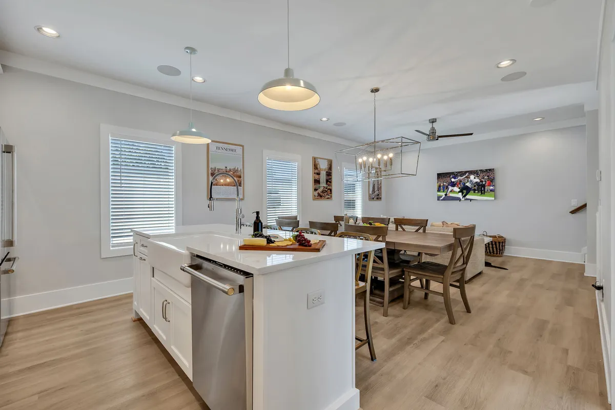A stylish interior featuring a kitchen island with bar stools, a nearby dining table, a chandelier overhead, and a wall-mounted TV. The space is inviting and communal, encouraging shared meals, casual chats at the bar, and group activities.