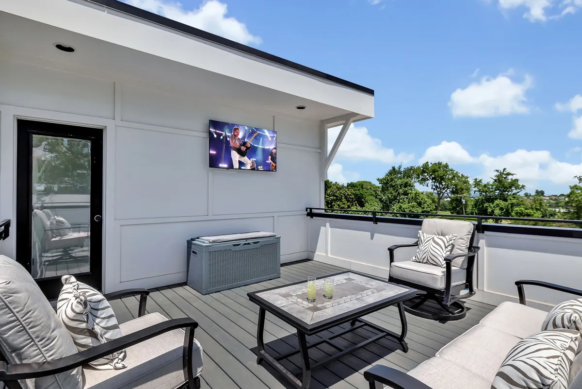 An exterior lounge area featuring comfortable seating, a wall-mounted TV, and greenery in the background, suggesting a relaxed environment for group entertainment, outdoor movie nights, or casual get-togethers.