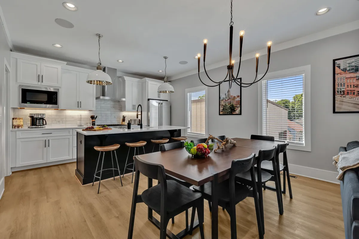 A chic, open-plan kitchen and dining area with a prominent kitchen island, formal dining table, modern chandelier, and distinctive wall art. The space is styled for both gourmet cooking and festive celebrations, echoing the elegance and functionality described in the section.