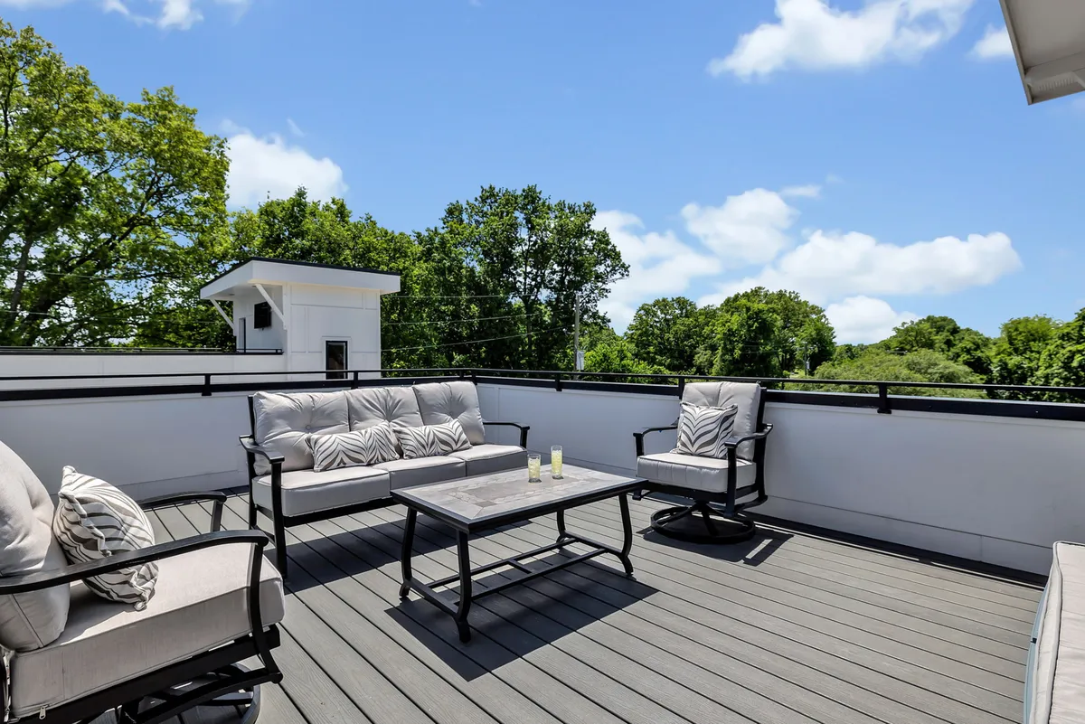A comfortable rooftop seating arrangement with a coffee table, accented by lush greenery in the background. The inviting setup suggests an intimate space for small group conversations, sunset views, or unwinding above the city.