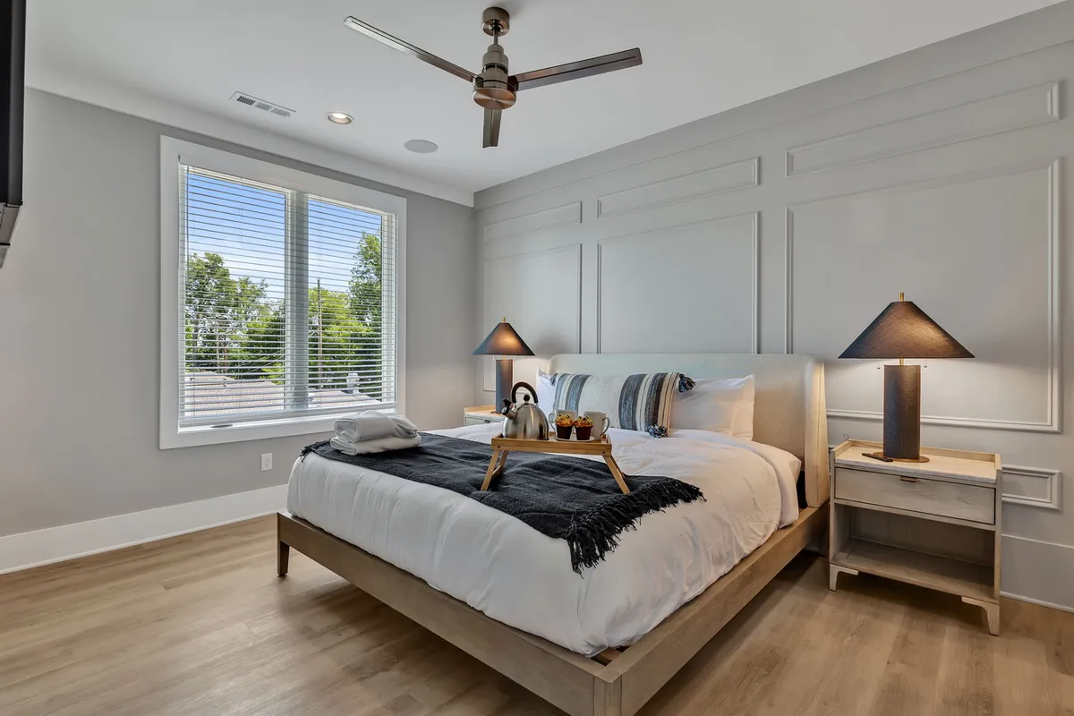 A calm, sunlit bedroom with a comfortable bed, nightstands, and a window letting in natural light. Subtle decorative elements create an inviting and cozy atmosphere.