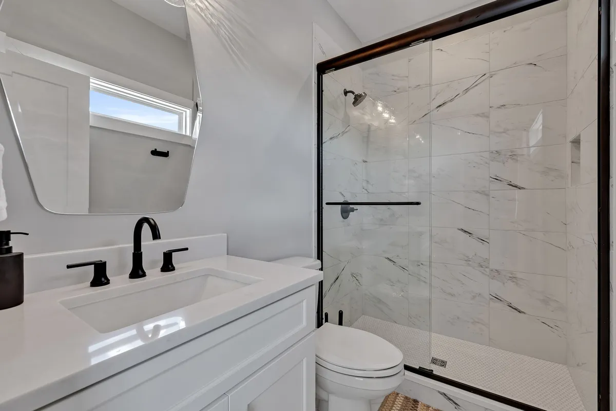 A serene, modern ensuite bathroom featuring a vanity with a sink, a glass shower enclosure, and a large mirror. The space feels spa-like and inviting, ideal for relaxation and daily routines.