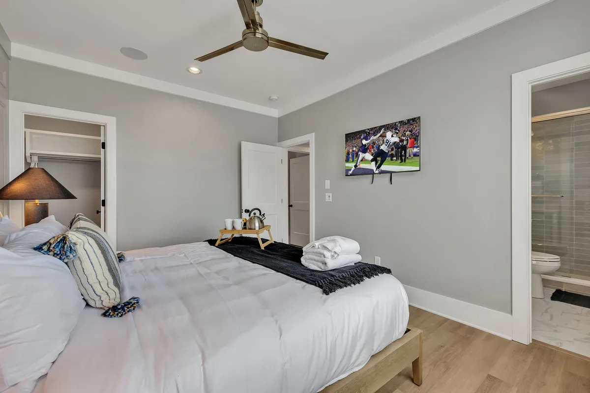 A comfortable bedroom featuring a large bed with plush pillows, a TV mounted on the wall, and a nightstand with a lamp. The room exudes warmth and relaxation, perfect for unwinding after a long day.