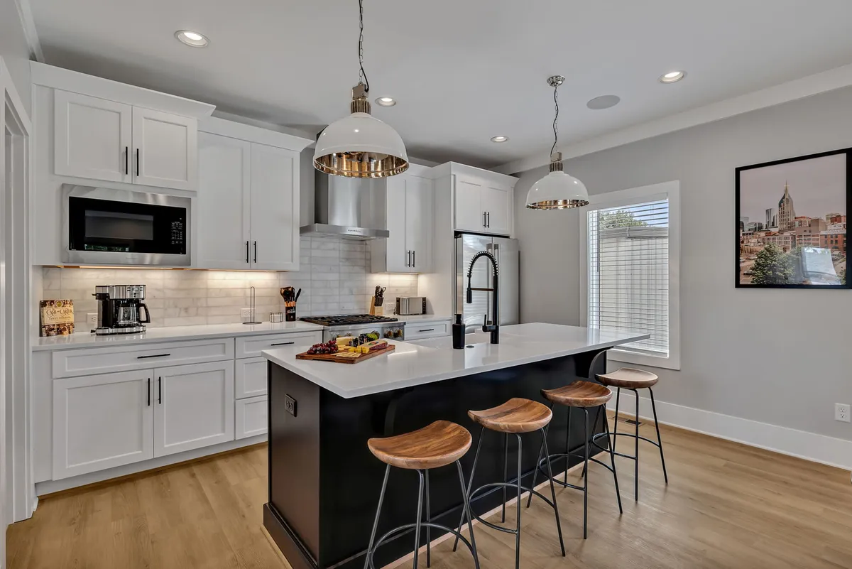 A bright, modern kitchen with a prominent island surrounded by stools, high-end appliances, and statement lighting. The space is open and designed to facilitate both meal preparation and social gatherings.